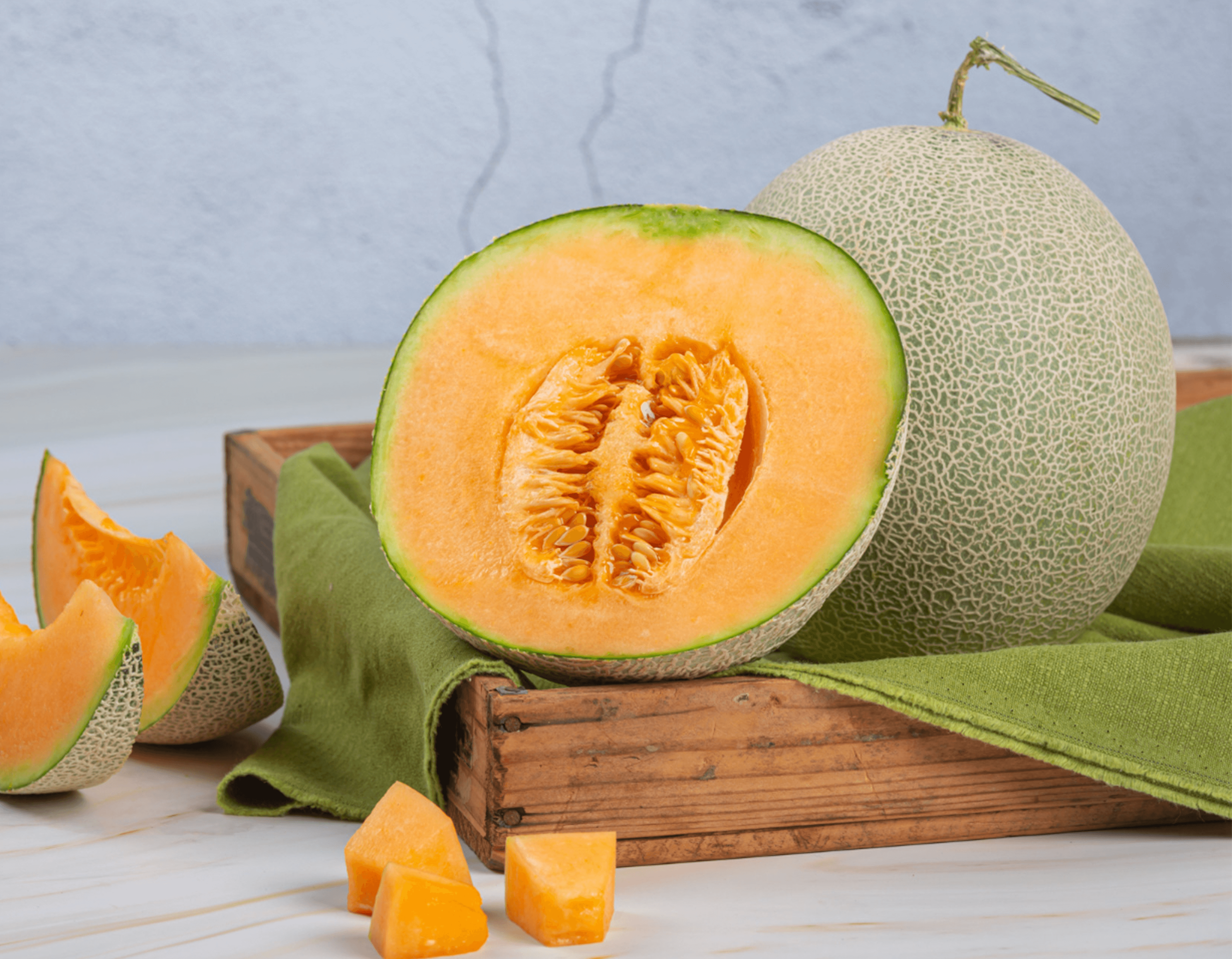 Fresh cantaloupe whole, halved and cubed in a wooden crate