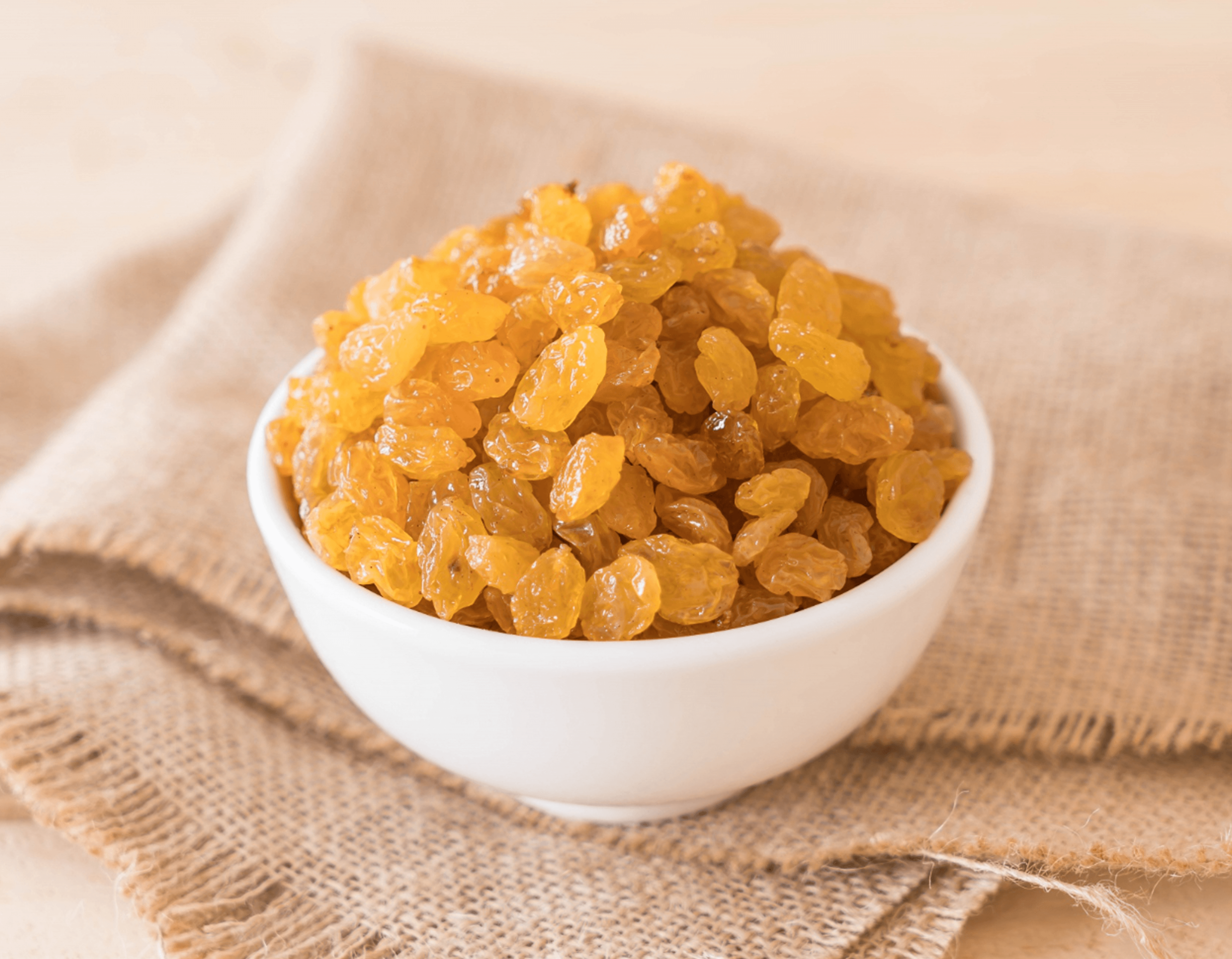 Golden raisins in a white ceramic bowl on natural fabric