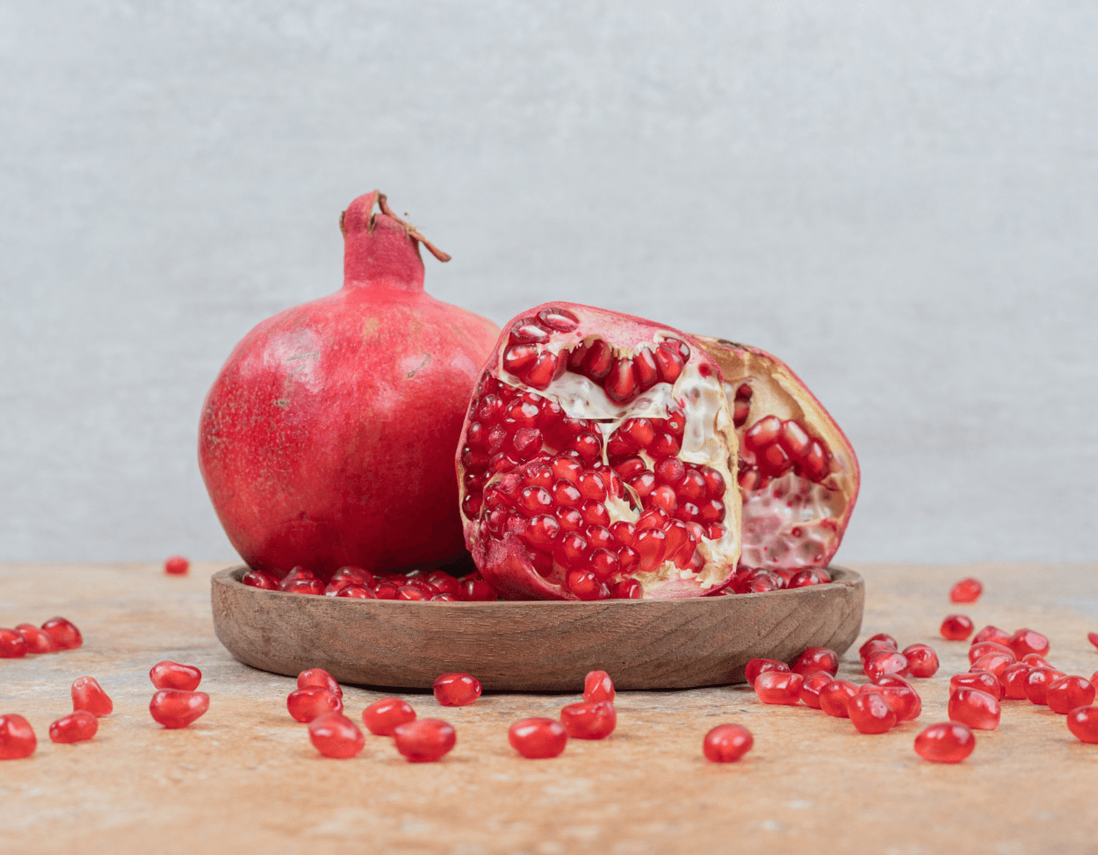 Fresh pomegranates with vibrant red arils on a wooden plate