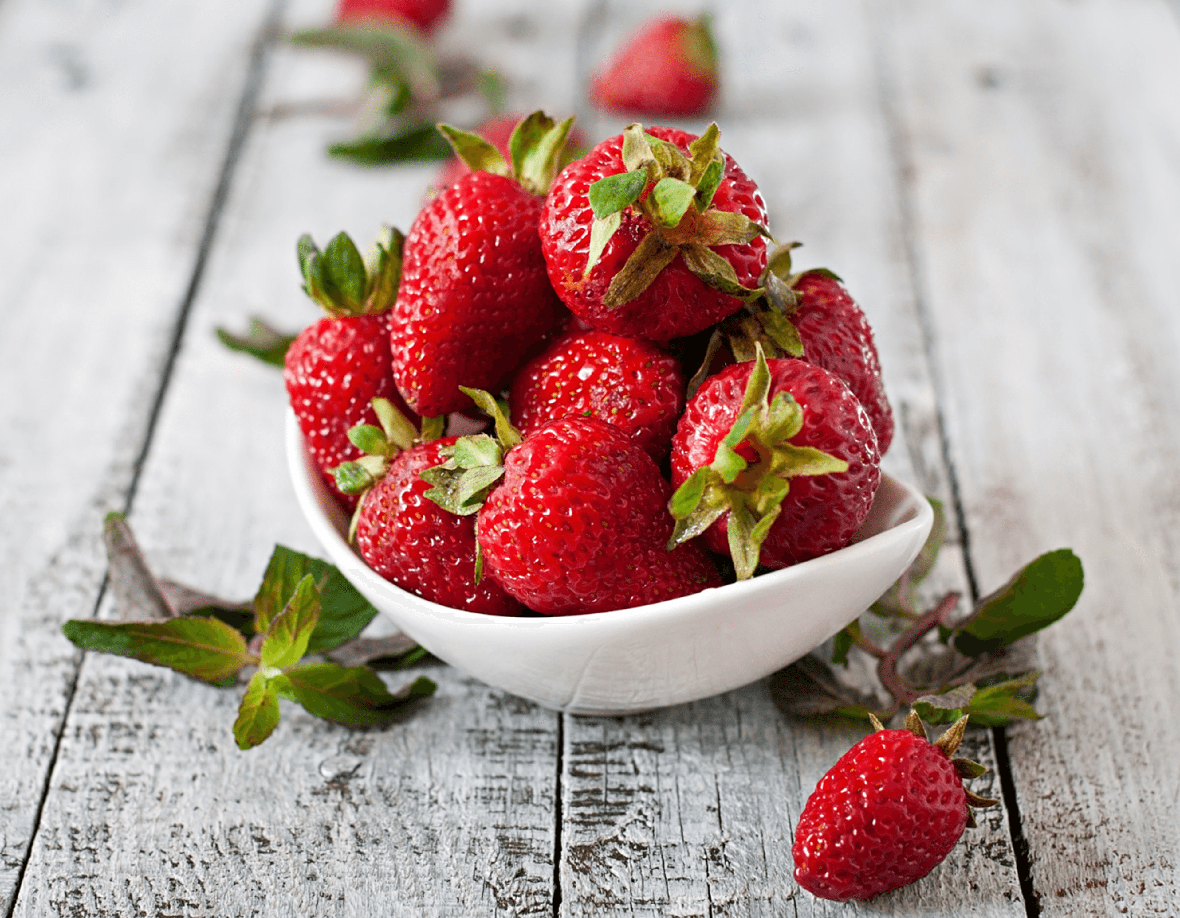 Fresh strawberries piled in a white bowl on a rustic wooden surface