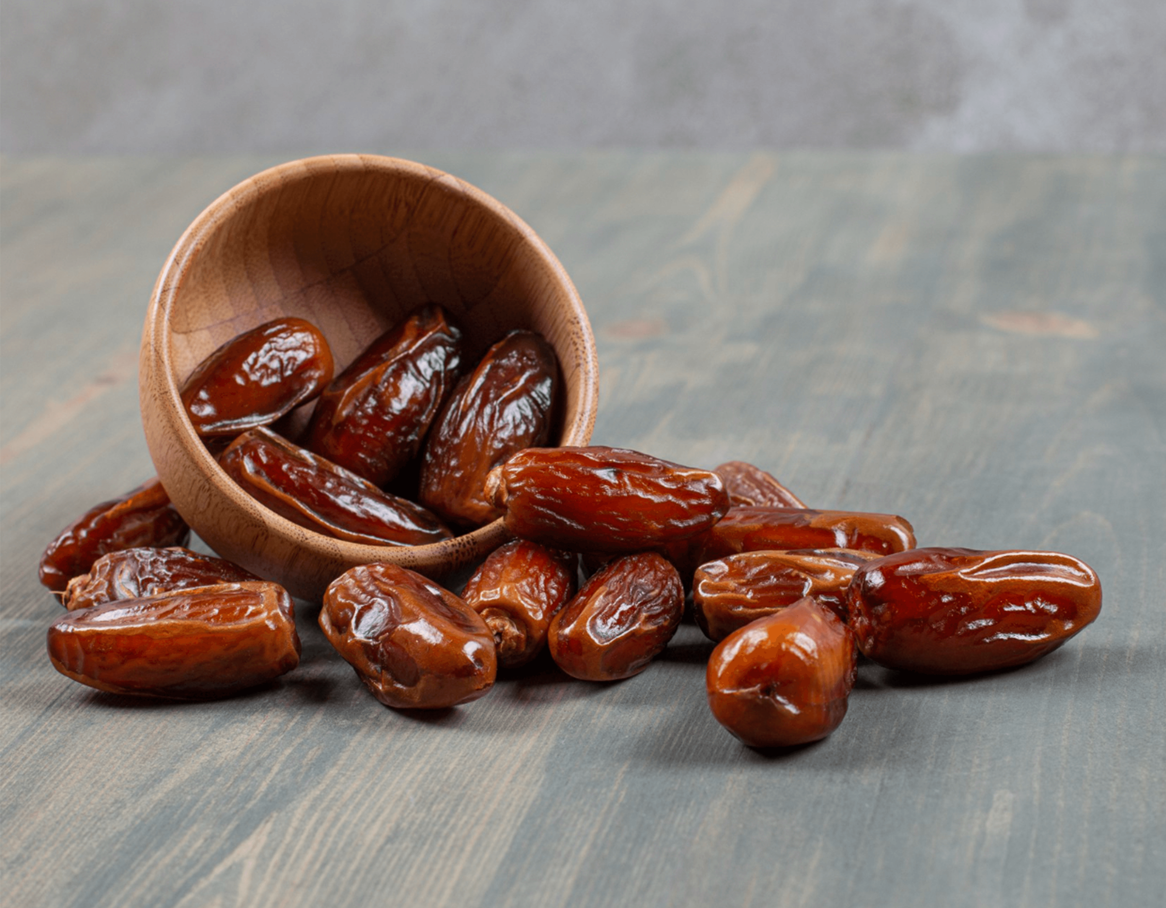 Glossy dates spilling from a wooden bowl onto a rustic surface